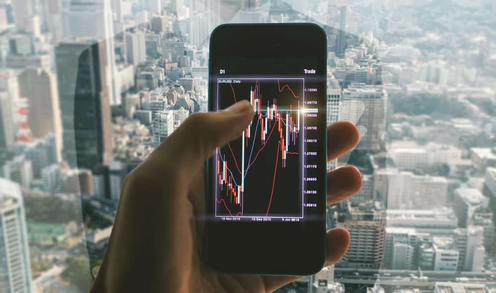 Business man making trading from his office. Close up on the smart phone with trading chart